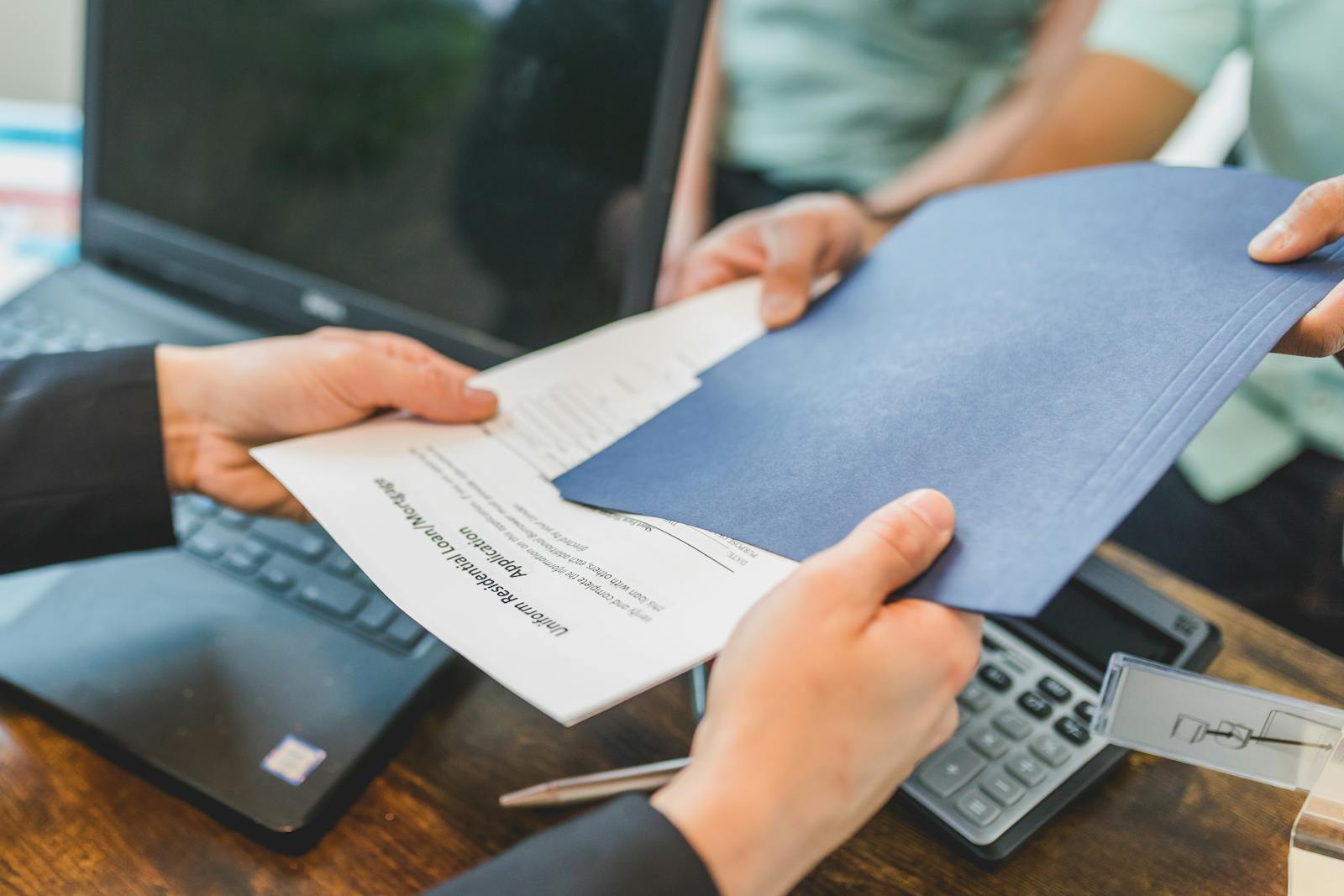 financial support, Close-up of hands exchanging real estate documents in an office setting.